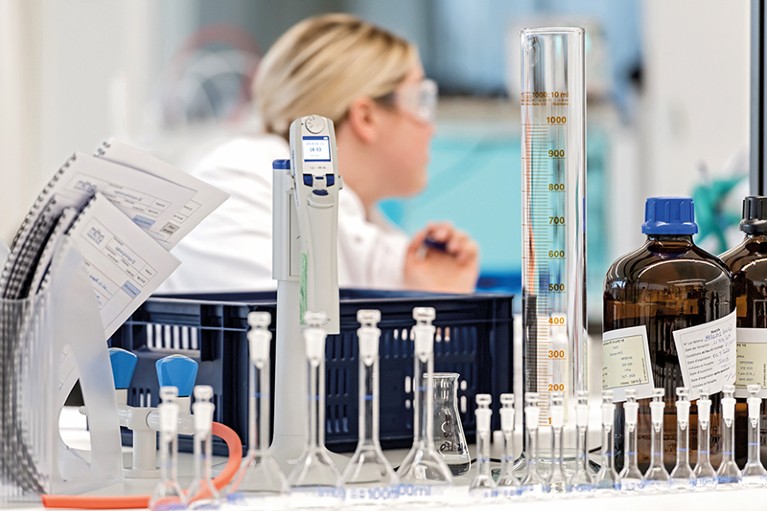 A female researcher sits behind a lab bench covered in glass flasks