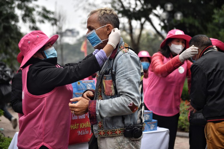 Volunteers wearing pink hats and tabards put surgical face masks on tourists arriving in Hanoi, Vietnam