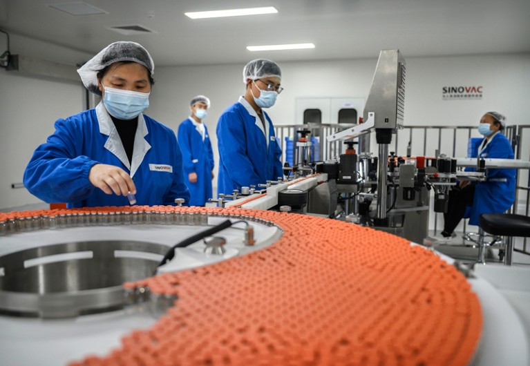 工人在蓝色工作服、口罩和发罩工作在生产线上检查瓶在中国的疫苗