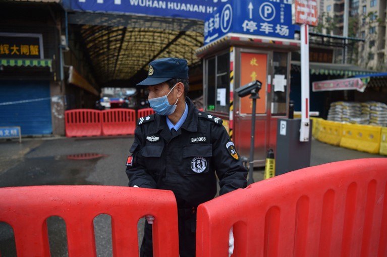 A policeman wearing a face mask stands behind red barriers at the entrance of a large covered market
