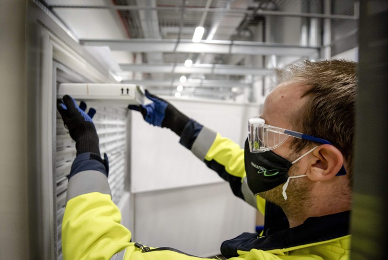A medical worker wearing a facemask, protective goggles and gloves stores a container of vaccines into a refrigeration unit