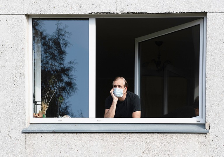 Man wearing a face mask looking out of a window