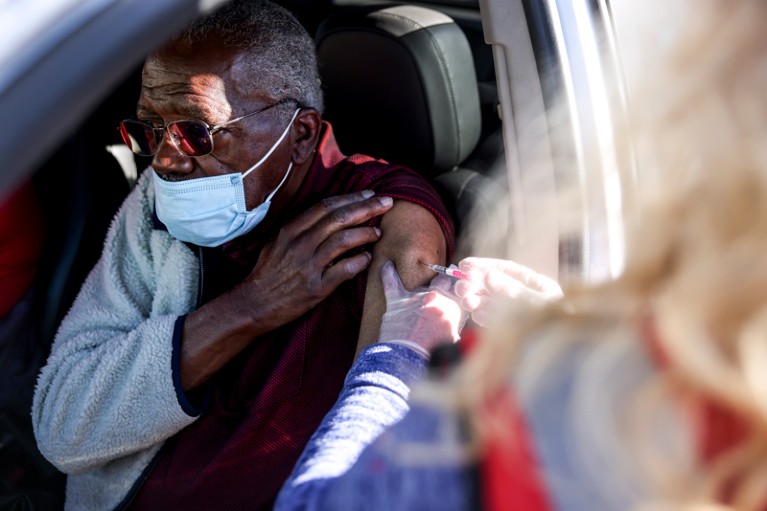 A health0care worker administers a vaccination through a car window to an older man