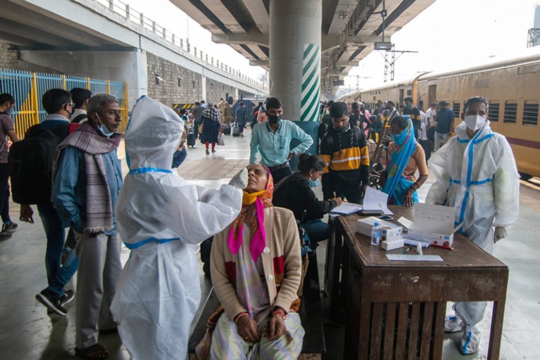 A healthcare worker conducts swab tests of train travelers for coronavirus infection in Mumbai, India