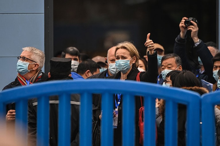 Researchers in face masks cluster behind a blue barrier.
