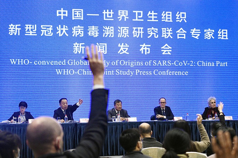 A panel in front of a blue screen with Chinese and English writing on it. People in the crowd are raising their hands.