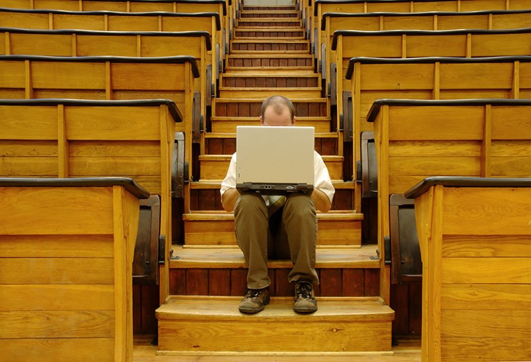 A man sits alone with a laptop in a university hall.