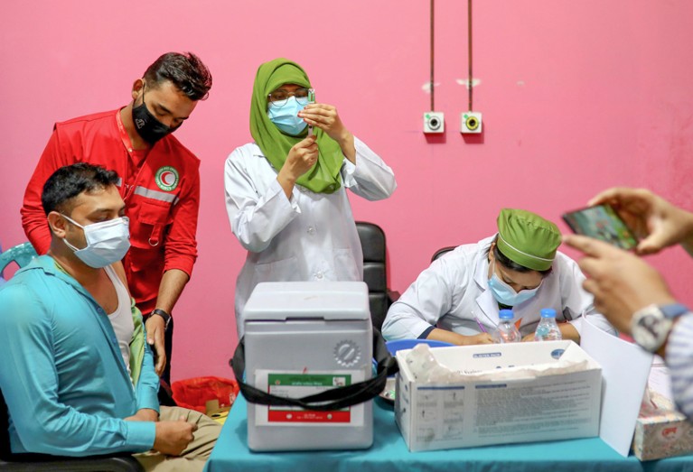 A man sits while medical workers prepare vaccines.
