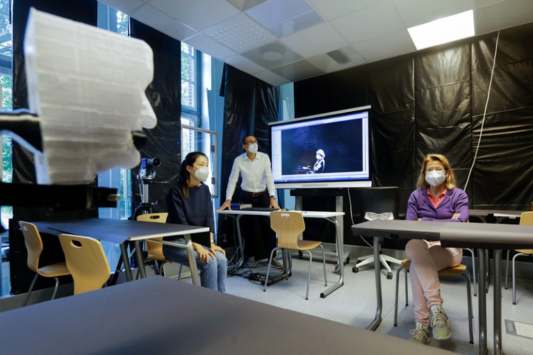 Three researchers in a room with desks and chairs with black sheeting on the walls and a mannequin head