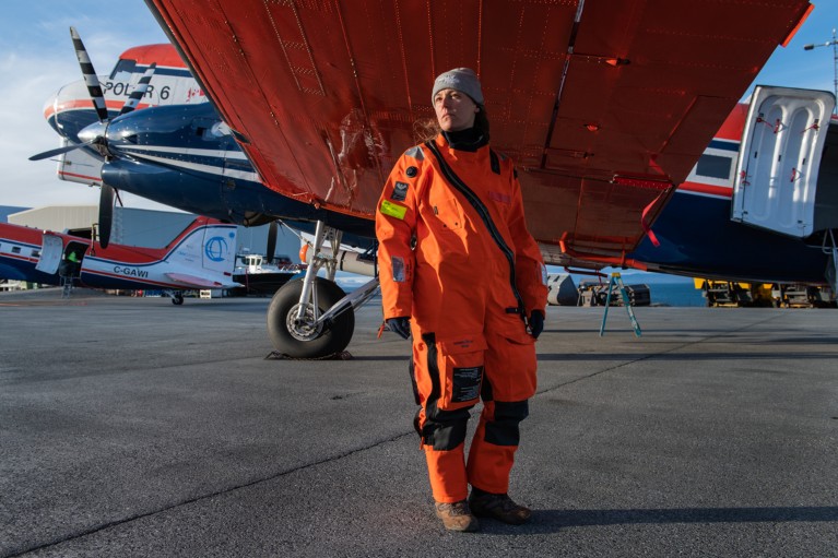 Cristina Sans Coll wearing an orange jumpsuit poses for a portrait beneath the wing of a plane