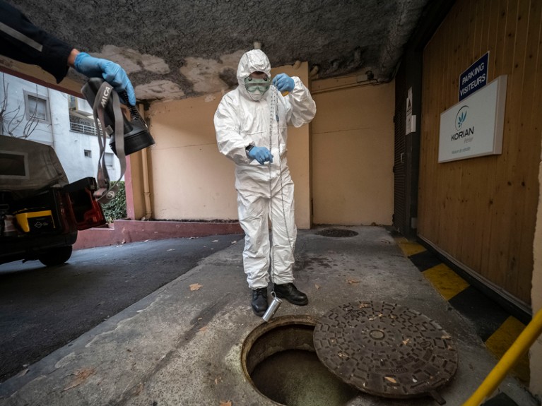 A firefighter wearing a protective suit takes samples from Marseille sewage water