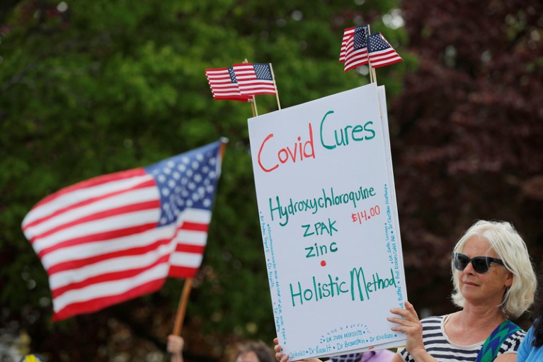 A woman holds a sign listing "Covid Cures," including hydroxychloroquine at a protest event in the US