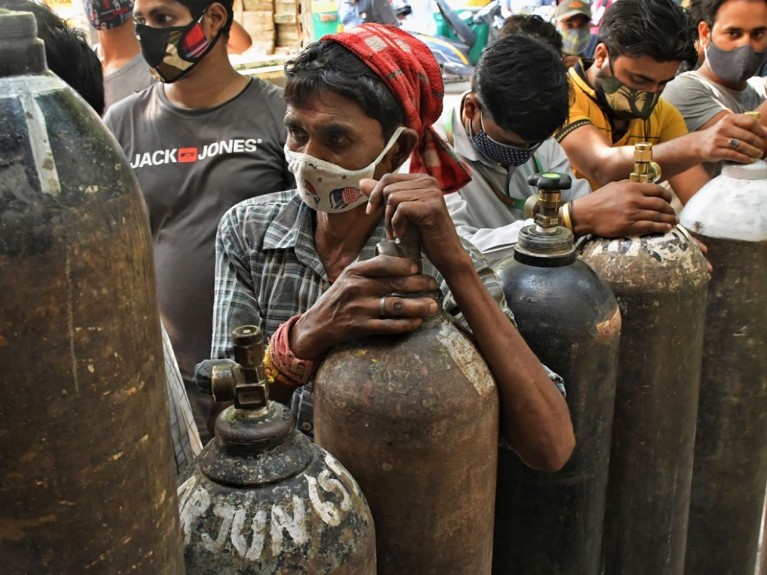 Masked people wait to refill oxygen cylinders.