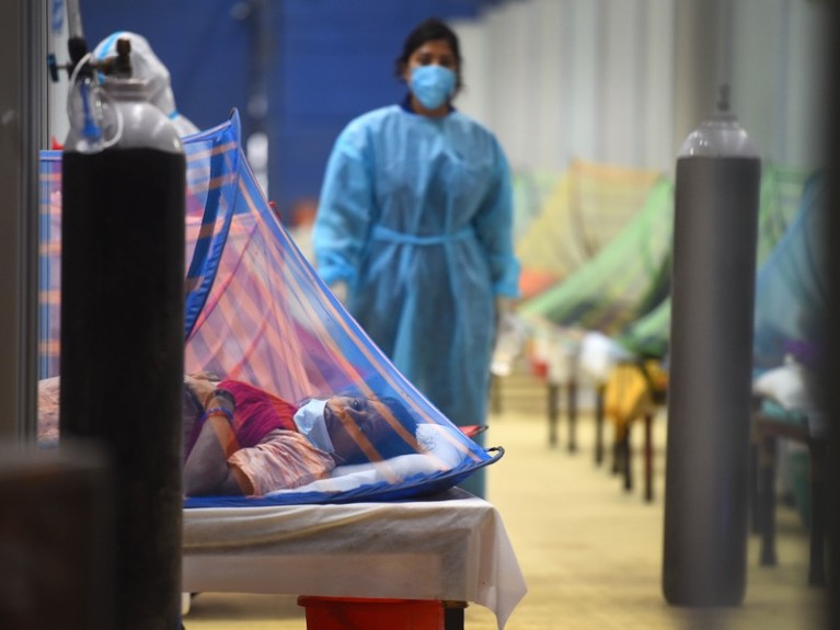 A masked health worker walks between hospital beds.