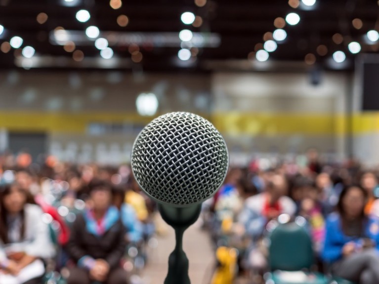 Microphone in front of a blurred audience in a conference hall.