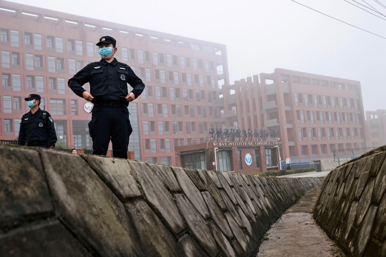 Security personnel in masks stand in front of an institutional building, in mist.