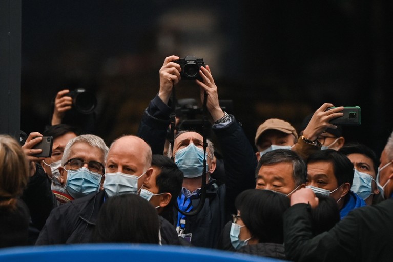 A crowd of people in masks, some taking photographs.