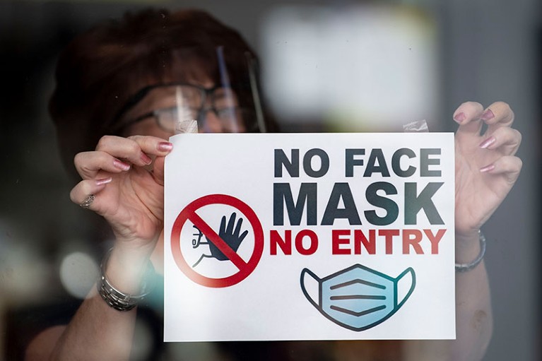 A woman puts a sign saying “no face mask no entry” in a shop window in Newport, Wales.