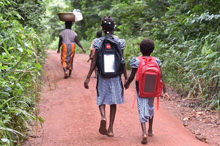 Ivorian schoolchildren walk to school carrying backpacks fitted with a connected lamp powered by solar panels