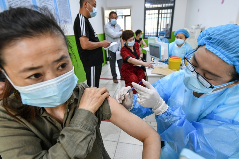 Masked health workers administer vaccines to masked people.