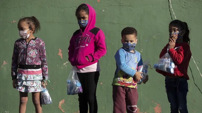 Four children in masks hold bags of supplies.