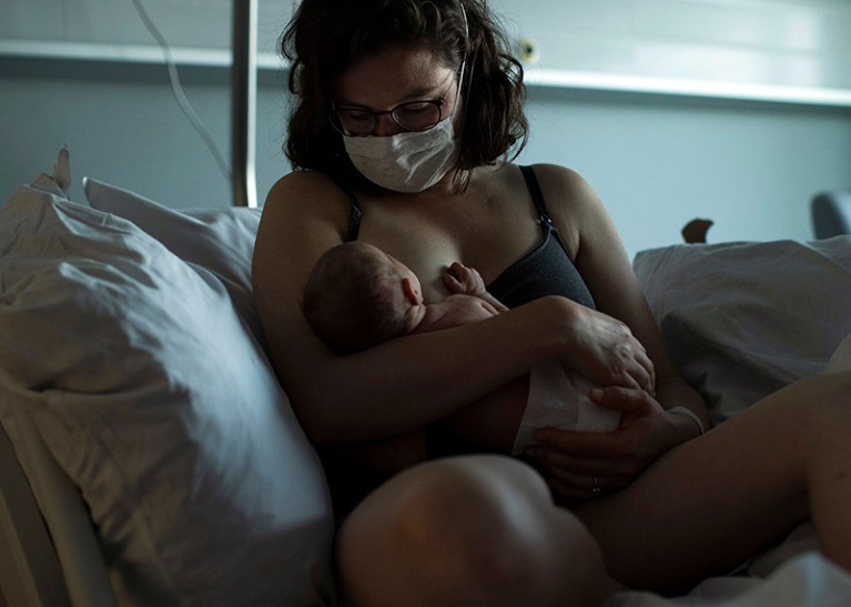 A mother, wearing a face mask to protect against the spread of coronavirus, breastfeeds her newborn child in a hospital