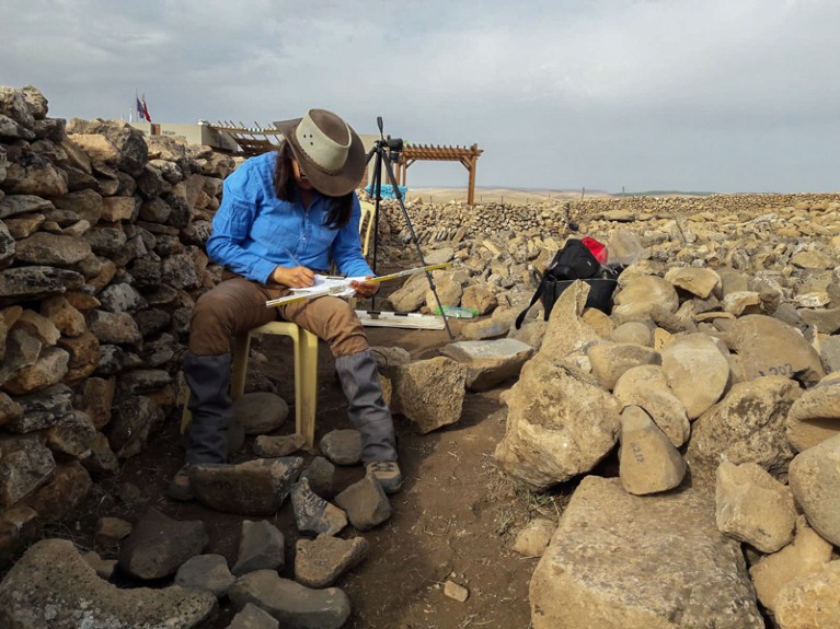 劳拉·迪特里希(Laura Dietrich)坐在一块岩石周围，在土耳其Göbekli特佩考古遗址(Tepe archaeological site)记录研磨石头