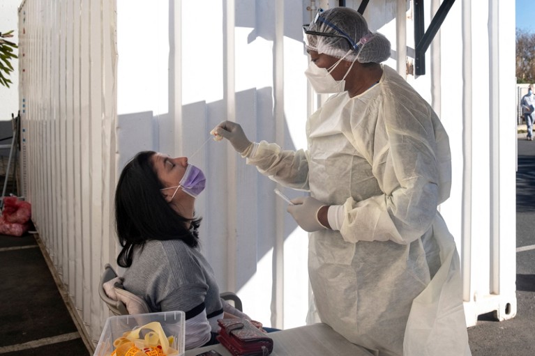 A woman receives a nasal swab from a health worker wearing personal protective equipment