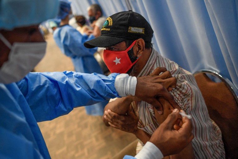 An elderly man wearing a red face covering receives a vaccine from a healthcare worker in Caracas, Venezuela