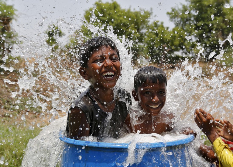 Two smiling young boys sit in a blue plastic container filled with water