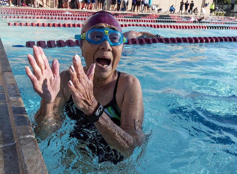 An older woman in a swimming pool, clapping to celebrate her victory in a race.