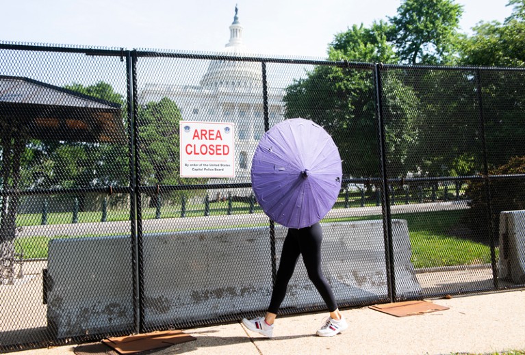 A woman walking past a gate outside the Capitol Building in Washington D.C. shields herself from the sun with a parasol