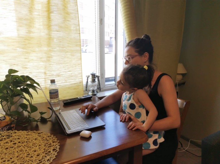 Yhasmin Moura sits at her table working on her laptop with her child on her lap