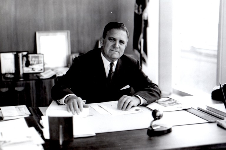 Black and white image of James Webb sitting at a desk.