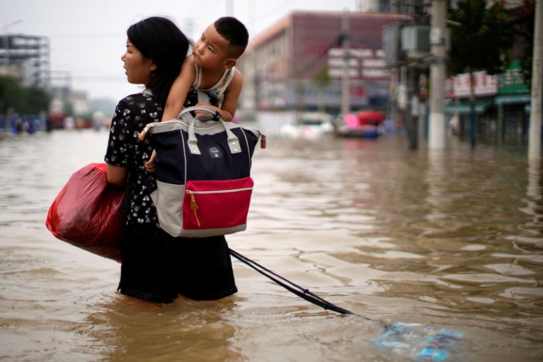 A woman carrying a child and belongings on her back wades through floodwaters in a city in China