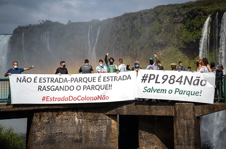 Protestors against a road through Iguaçu National Park in Brazil stand on a platform with signs in front of Iguaçu Falls.