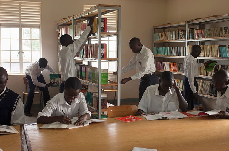 Several student teachers in the library, reaching for books or studying, at Fort Portal Teacher Training College in Uganda.