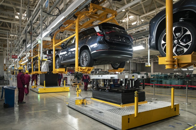 Employees install batteries into elevated cars on the production line of an electric vehicle production facility in China