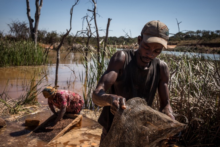 A woman and a man separating cobalt from mud and rocks by a river in the Democratic Republic of Congo