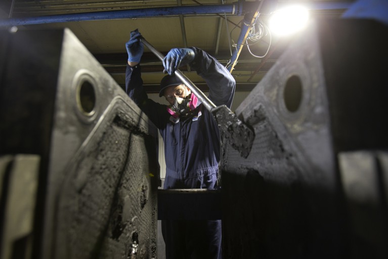 A worker scrapes black mass off metal plates at the Li-Cycle lithium-ion battery recycling facility