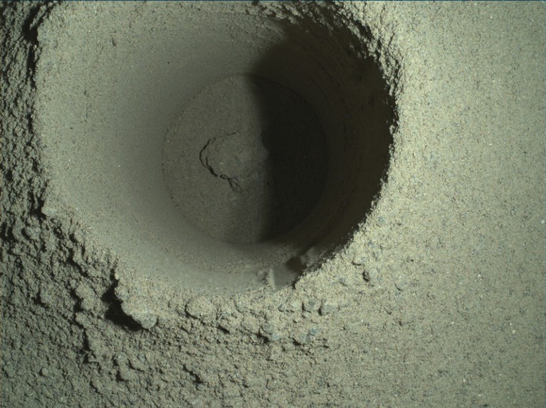 View from above of a hole drilled in rock, with crumbled material at the bottom.