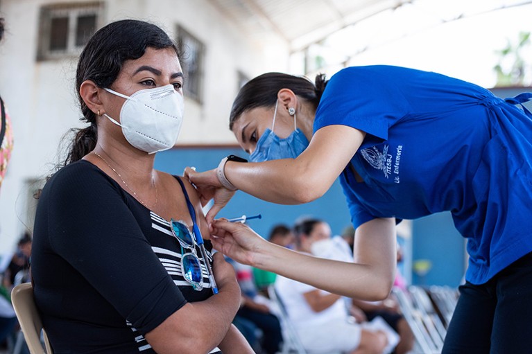 A health worker administers a dose of the AstraZeneca vaccine to a patient waiting on a chair in Mexico City, Mexico.
