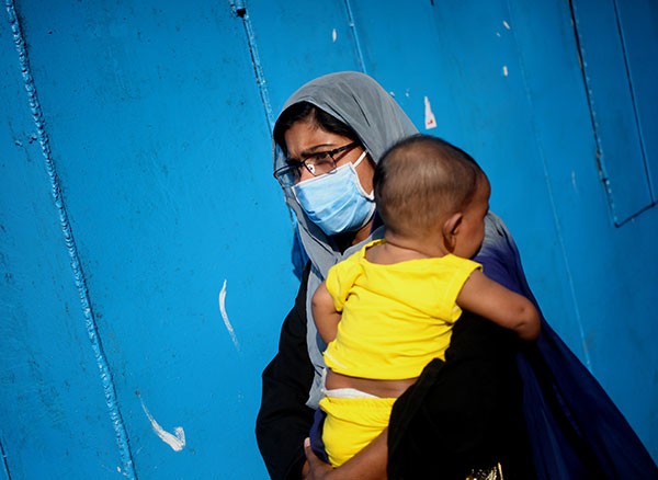A woman wears a mask whilst carrying a child at a ferry terminal in Dhaka, Bangladesh.