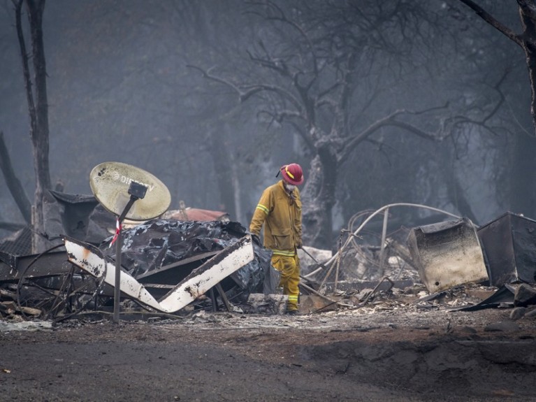 A firefighter stands amid the burnt remains of a house