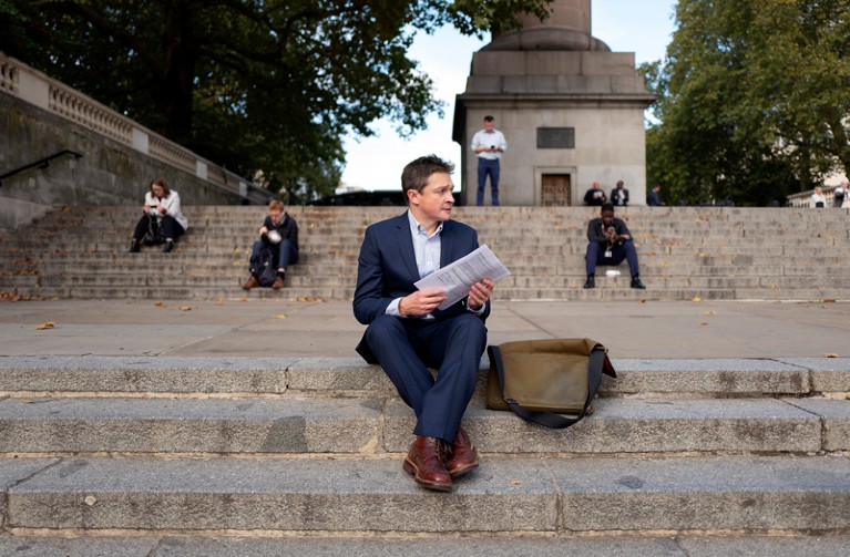 Daniel Bose sitting on some stone steps holding a sheaf of paper as he prepares to go before a panel to get approval for a grant