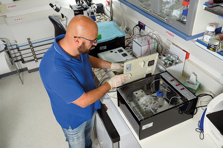 Jacob Hanna stands at a lab bench working on some equipment