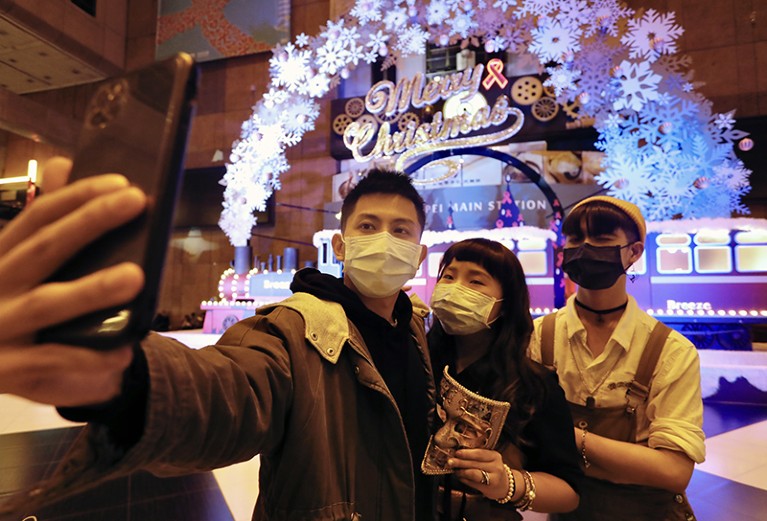 Three people pose for a photo while in masks during an indoor holiday event in Taipei, Taiwan.