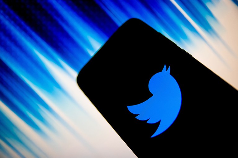 The Twitter logo is displayed on a black smartphone with a background of blue and white stripes.