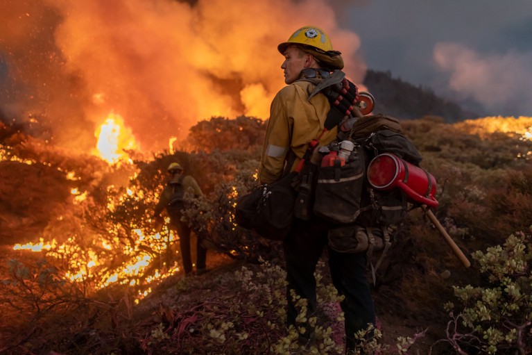 Firefighters laden with equipment approach part of a burning forest fire near Caldor California