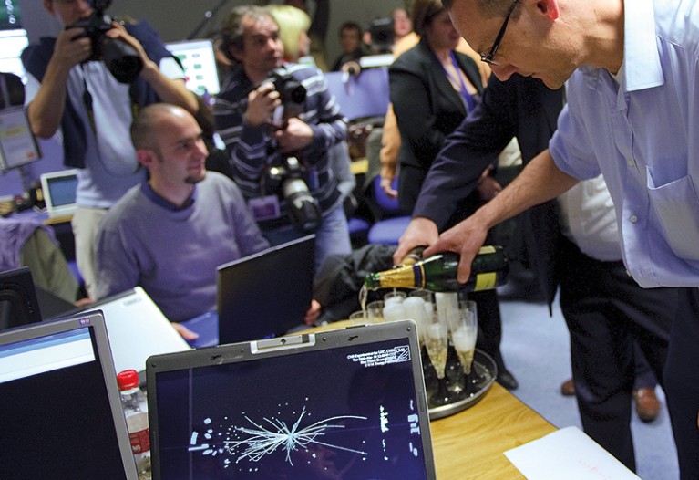 A person pours champagne into some glasses on a tray amid a group of cnference attendees